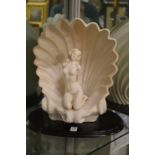 An Art Deco style table lamp modelled as a seated female nude within a shell on a wooden base.