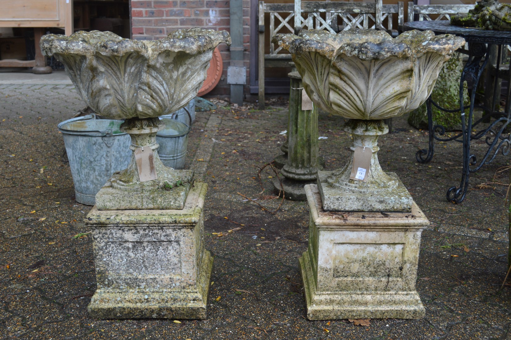 A pair of composite pedestal garden urns on square bases (one damaged).