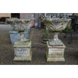 A pair of composite pedestal garden urns on square bases (one damaged).