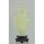 A CHINESE CARVED JADE LIDDED VASE AND WOODEN STAND, the vase with foo dog finial and drop ring