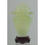 A CHINESE CARVED JADE LIDDED VASE AND WOODEN STAND, the vase with archaic style carving and drop