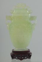 A CHINESE CARVED JADE LIDDED VASE AND WOODEN STAND, the vase with archaic style carving and drop
