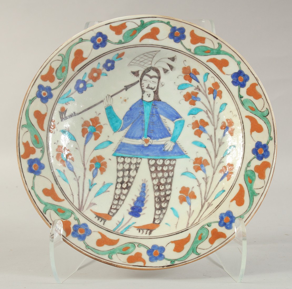 A TURKISH OTTOMAN GLAZED POTTERY PLATE, painted with a figure and flora, 31.5cm diameter.