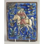 A PERSIAN QAJAR GLAZED POTTERY TILE, depicting a figure on horseback and flora, inset within an