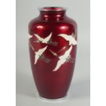 A JAPANESE ANDO RED GROUND CLOISONNE VASE, decorated with enamelled cranes, the rims with white