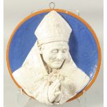 A CONTINENTAL GLAZED POLYCHROME TERRA COTTA ROUNDEL of a praying Bishop on a blue background. 32cm