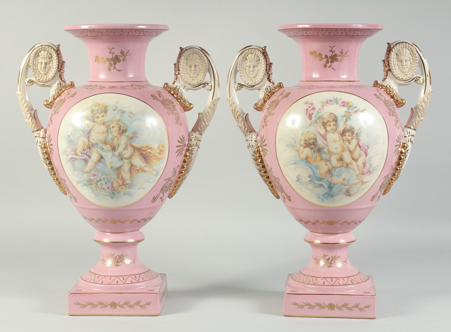 A PAIR OF SEVRES STYLE PINK TWO HANDLED VASES with oval panels of cupids. 1ft 4ins high.