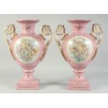 A PAIR OF SEVRES STYLE PINK TWO HANDLED VASES with oval panels of cupids. 1ft 4ins high.