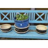 A blue glazed plant pot with plants and a set of three black glazed planters with bases.