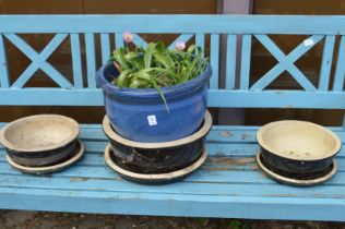 A blue glazed plant pot with plants and a set of three black glazed planters with bases.
