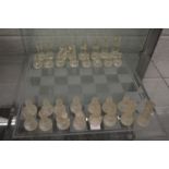 A glass chess board and various pieces (not a complete set).