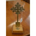 A brass cross on a wooden base, the base set with various gem stones.