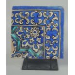 A PERSIAN QAJAR GLAZED POTTERY CORNER TILE, on a fitted metal stand, the tile painted with foliate