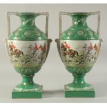 A PAIR OF SEVRES DESIGN GREEN GROUND HUNTING VASES with looped handles on square bases.