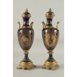 A PAIR OF SEVRES DESIGN DEEP BLUE PORCELAIN AND GILT METAL VASES AND STANDS. 18ins high.