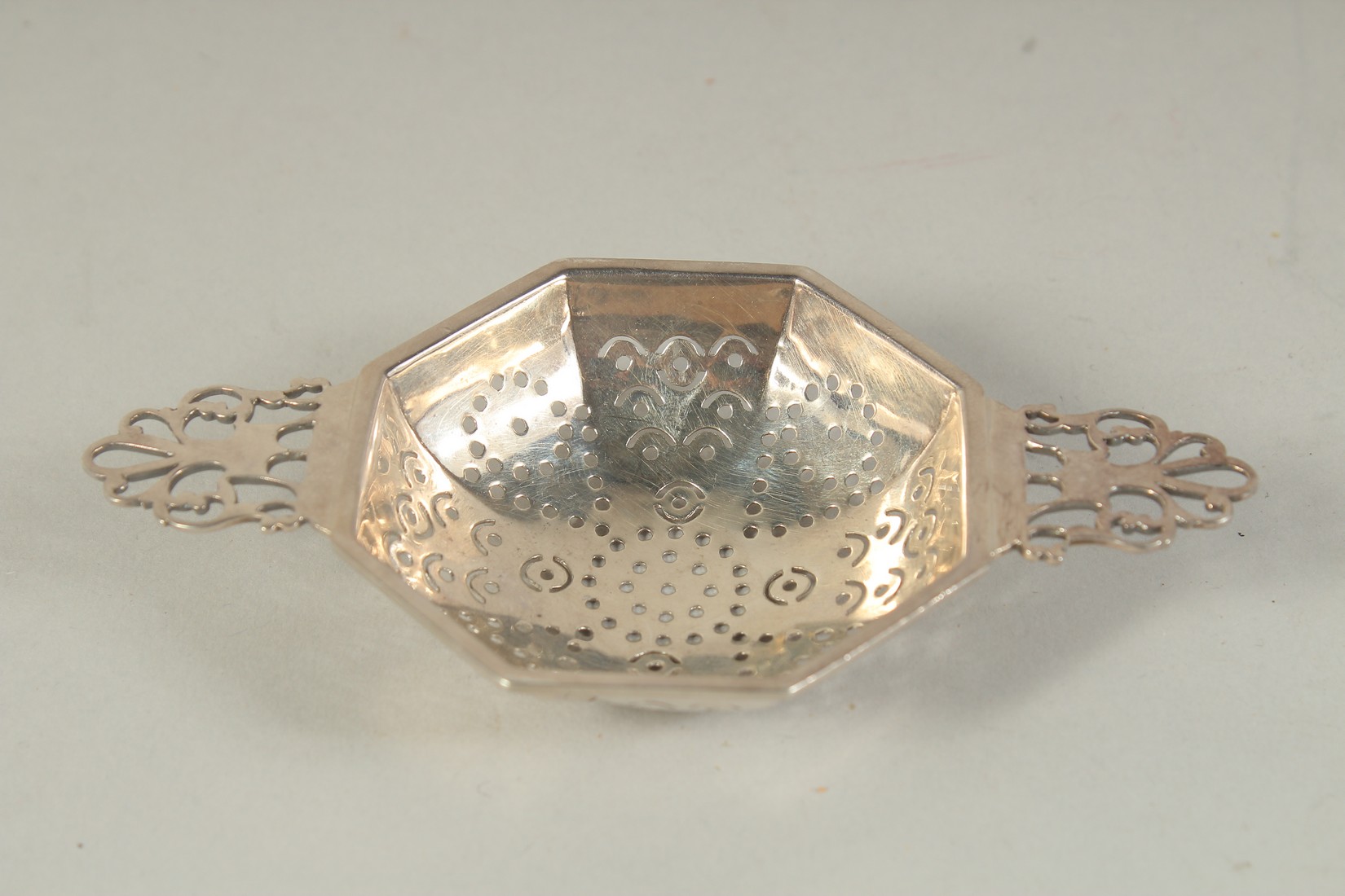 A TWO HANDLED SILVER TEA STRAINER.