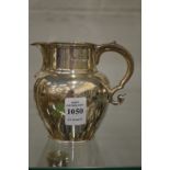 A silver cream jug with scroll handle.