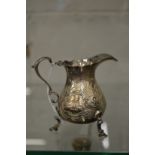 A small silver cream jug with embossed decoration.