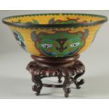 AN UNUSUAL CHINESE YELLOW GROUND CLOISONNE BOWL, on hardwood stand, bowl 23cm diameter.