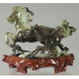 A CHINESE CARVED GREEN HARDSTONE GROUP OF HORSES, on a fitted hardwood stand, 17cm wide.