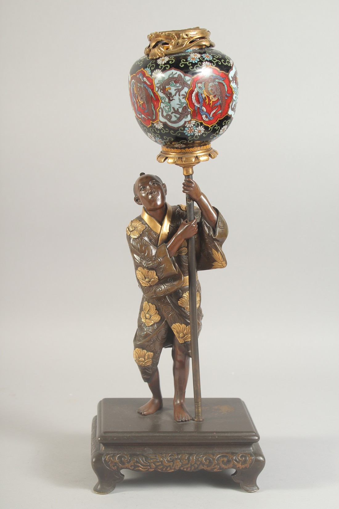 A FINE JAPANESE MEIJI PERIOD BRONZE OKIMONO holding a cloisonne urn aloft, the figure with gilt