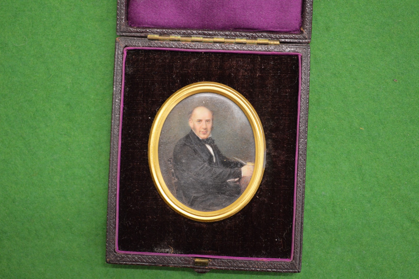 A portrait miniature of a Gentleman seated at a desk in a leather travelling case.