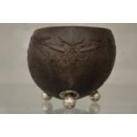 A carved coconut cup on three silver feet.