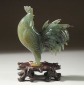 A CARVED JADE FIGURE OF A COCKEREL on a wooden stand, 11cm high (on stand).