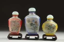 THREE CHINESE REVERSE GLASS PAINTED SNUFF BOTTLES, with wooden stands, each finely painted with