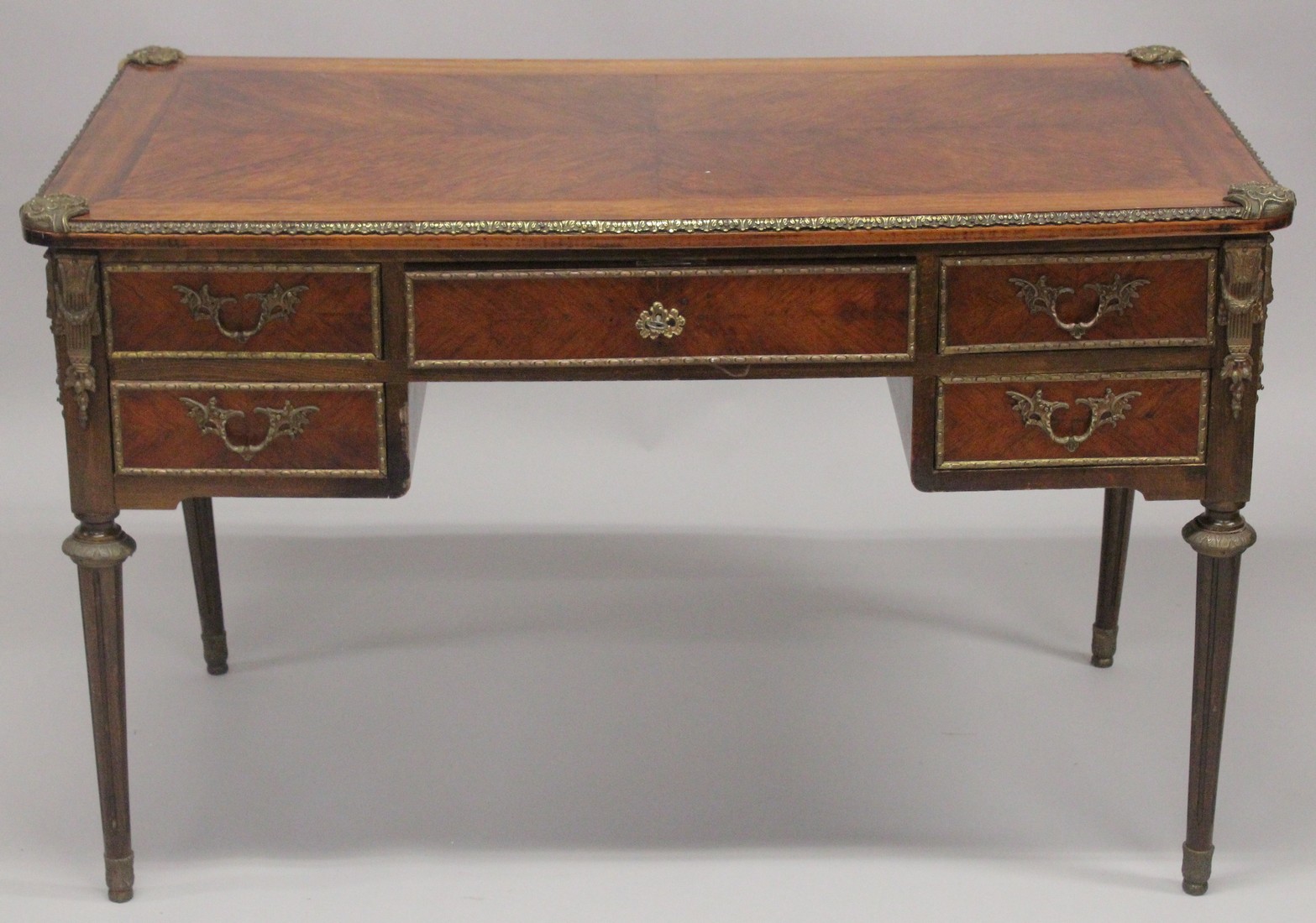 A LOUIS XVITH DESIGN WRITING TABLE with wooden top, five drawers on turned legs with ormolu