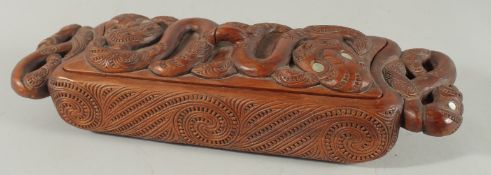 A MAORI LONG CARVED WOOD FOOD VESSEL carved with masks and mother of pearl eyes. 13ins high.