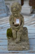 A small garden ornament modelled as a boy seated reading a book.