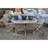 An oval garden table with six folding chairs, two with arms.