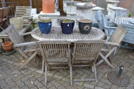 An oval garden table with six folding chairs, two with arms.