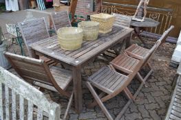 A rectangular wooden garden table with seven folding chairs.