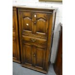 An oak cupboard with an arrangement of four panelled doors, brushing slide and a small drawer.