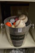 Fifty assorted golf balls and soft balls contained in an ice bucket.