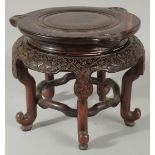 A LARGE CHINESE CARVED HARDWOOD STAND, with circular top, the skirt carved with bat motifs, elevated