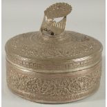 A MALAYSIAN EMBOSSED SILVER CIRCULAR BOX, with figural peacock finial and foliate decoration, 18cm