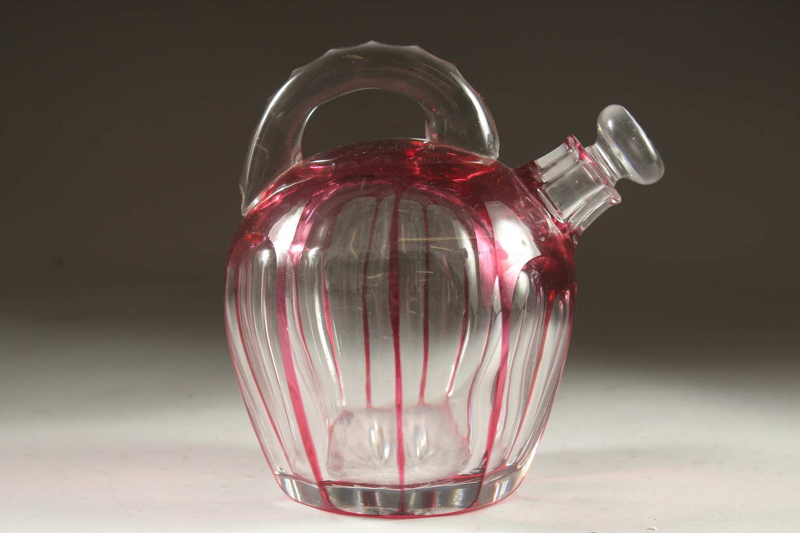 A SLICE CUT RUBY TINTED GLASS EWER with stopper. 7ins high.
