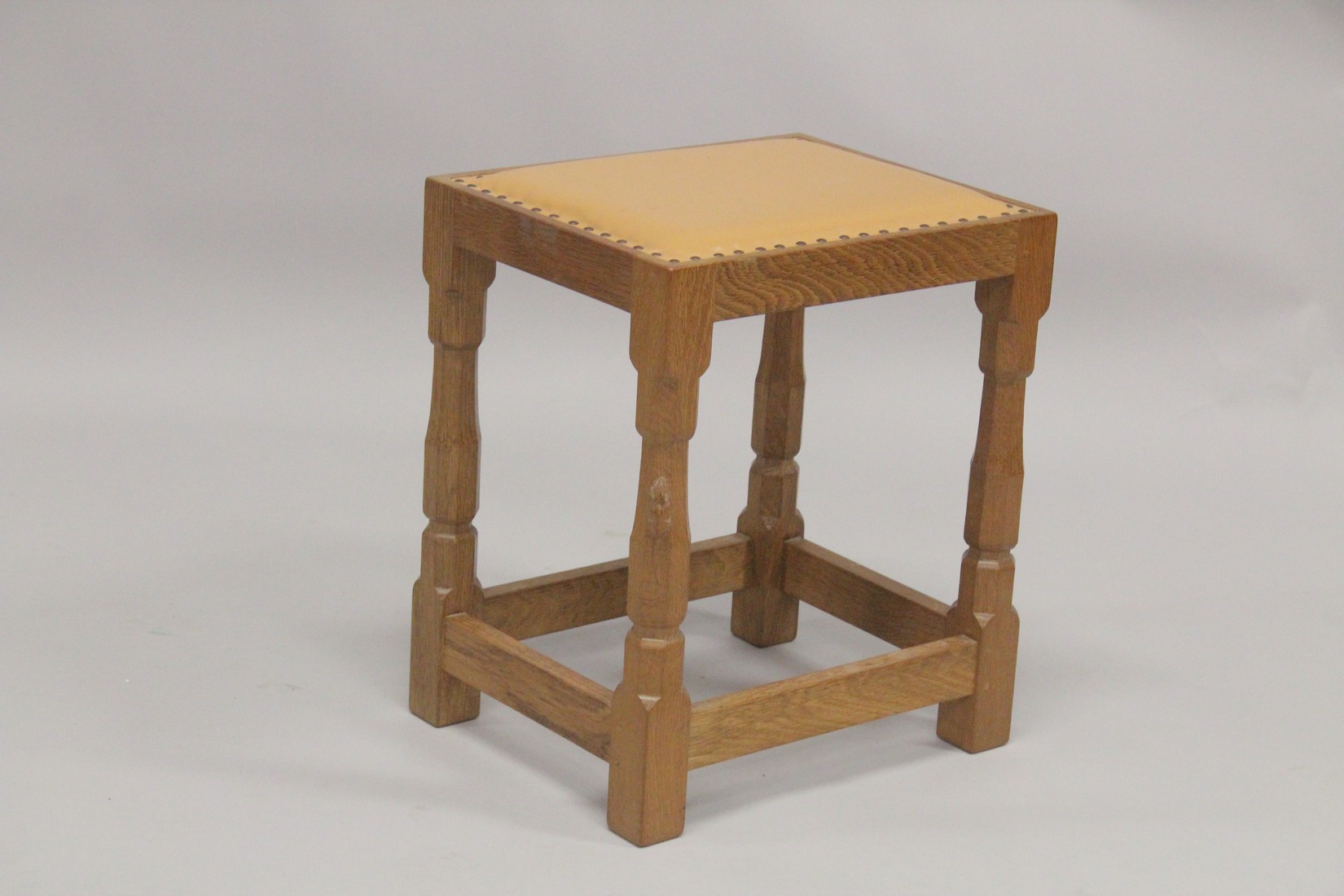 ROBERT "MOUSEMAN" THOMPSON. AN OAK STOOL with close nailed tan leather seat, on four stretchered