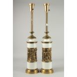 A PAIR OF TALL WHITE PORCELAIN AND BRASS LAMPS with a band of cupids. 27ins high.