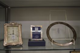 A silver mounted desk clock, small silver photograph frame and a silver circular frame.