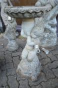 A composite bird bath the top supported by a seated child.