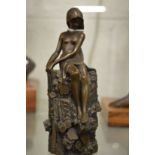 A small bronze of a female semi nude seated on a tree stump.