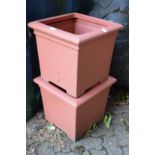 A pair of plastic square shaped garden planters.