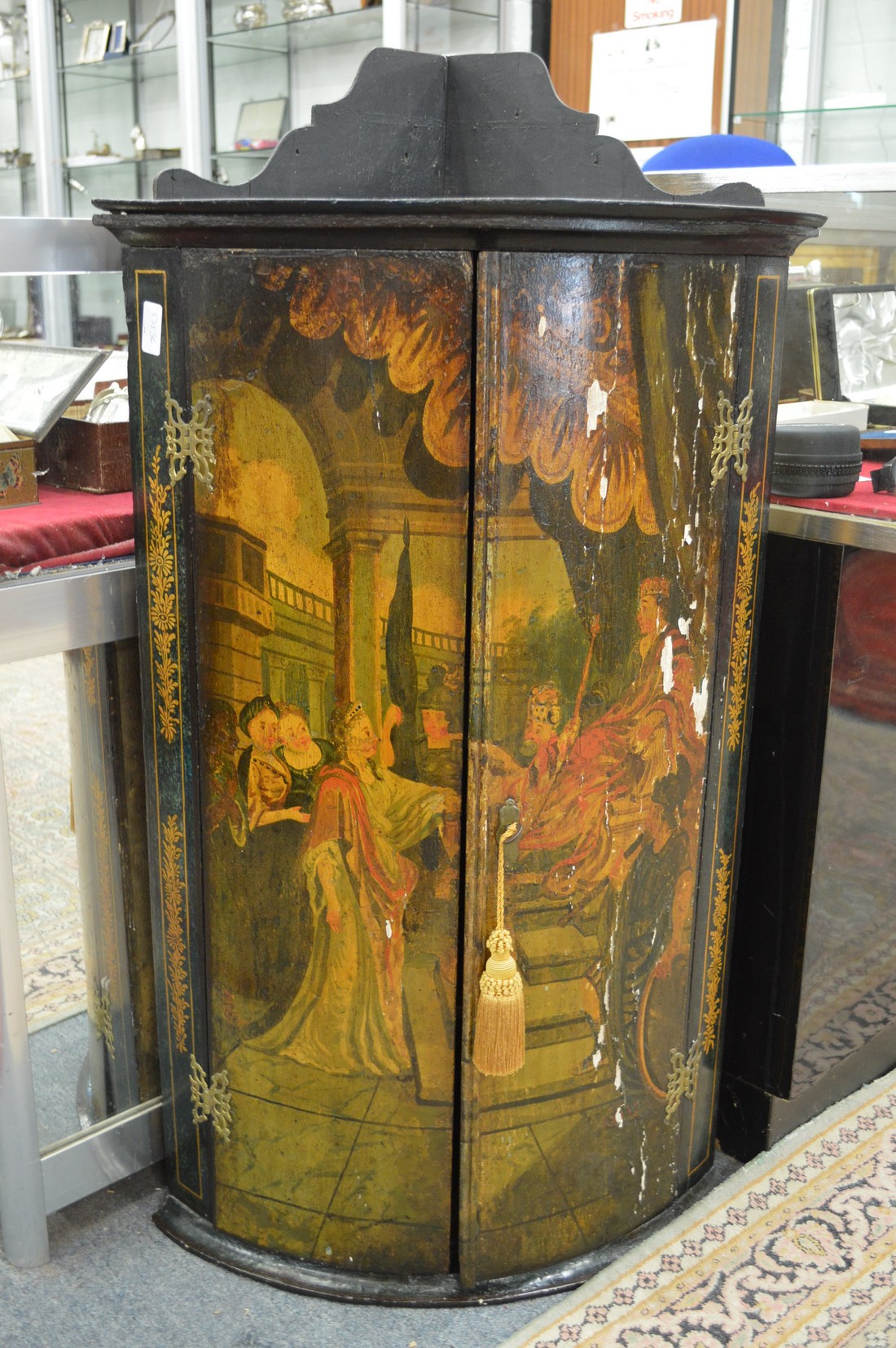 A George III lacquer bow front hanging corner cupboard with painted decoration depicting a classical