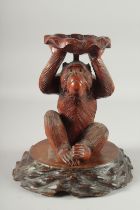 A CHINESE WOODEN CARVING OF A MONKEY holding a lily pad aloft, mounted to a carved hardwood base,