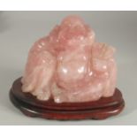 A CHINESE CARVED ROSE QUARTZ BUDDHA on wooden stand, 19cm wide overall.