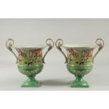 A PAIR OF SEVRES DESIGN GREEN GROUND TWO HANDLED URN SHAPED VASES with hunting scenes. 9ins high.